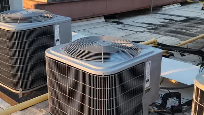 Commercial rooftop HVAC units and air conditioning condensers installed on a flat building roof in daytime.