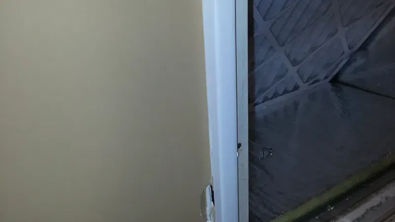 Close-up of an HVAC air filter frame installed in an indoor wall with visible dust and a small wall damage beside it.