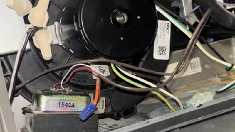 Internal view of HVAC unit showing motor, wiring, pipes, and warning labels inside the system.