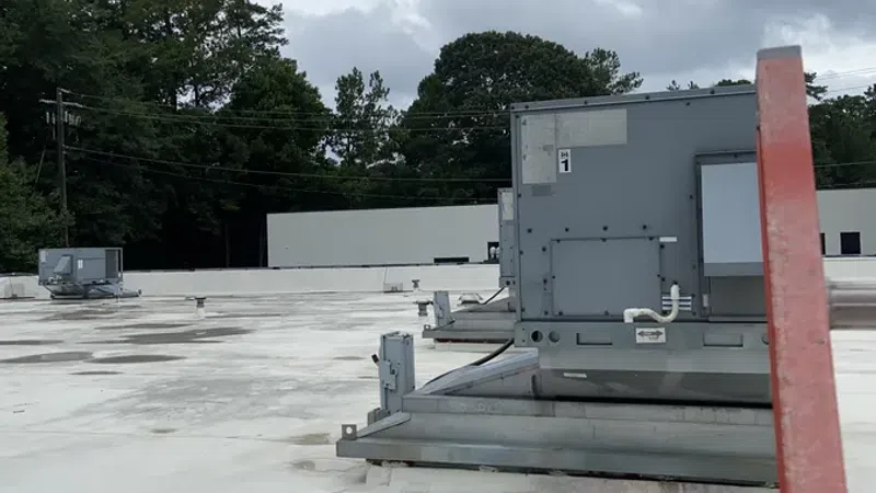 Commercial building rooftop with HVAC units mounted on a flat white roof under cloudy sky.