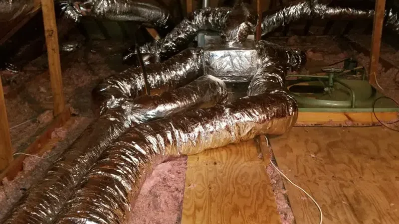 Shiny flexible air ducts installed in a wooden attic space with insulation and ventilation system components.