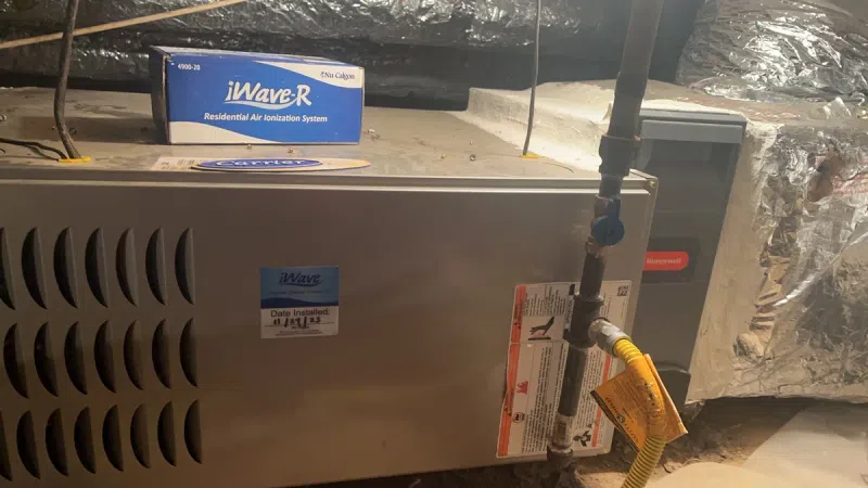 Residential air ionization system unit installed in an attic with connected pipes and air handler components.