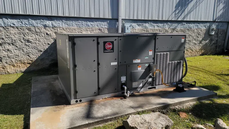 Outdoor Rheem commercial HVAC unit installed on concrete pad beside building casting shadows on grass.