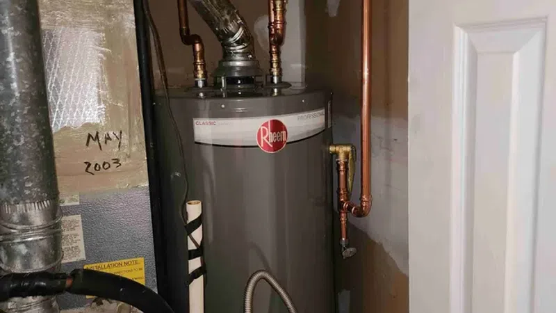 Gray Rheem water heater installed in a utility closet with yellow gas line and warning labels.