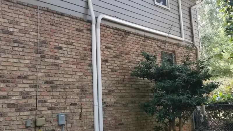 Exterior side of a house with brick and siding walls, two air conditioning units, and a small tree nearby.