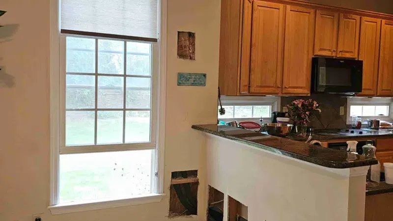 Interior view of a kitchen with wood floors, exposed wall cutouts, and wooden cabinets with a granite countertop.