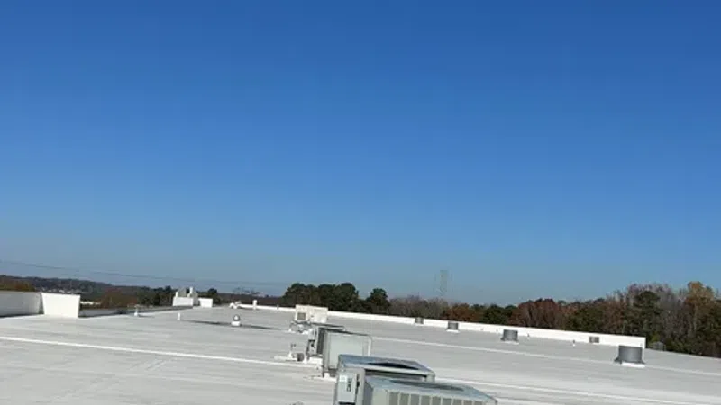 White commercial rooftop with multiple HVAC units under clear blue sky and distant tree line