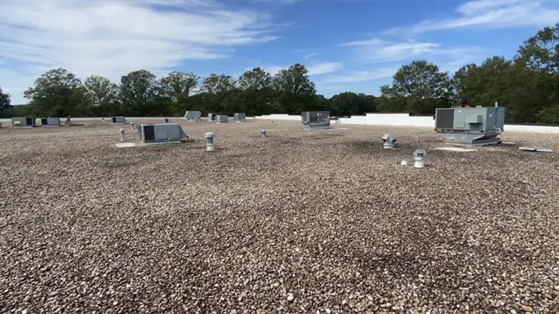 Flat commercial rooftop covered with gravel and HVAC units under a blue sky with scattered clouds.