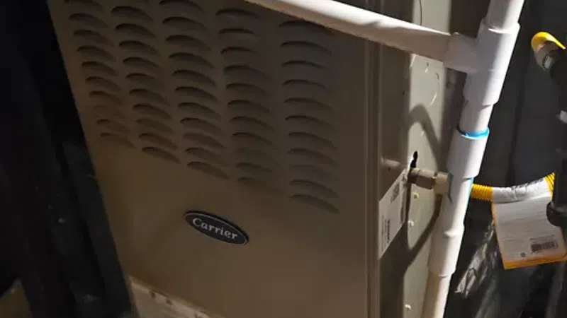Carrier brand furnace unit installed with attached PVC pipes and metal vent in a basement setting.