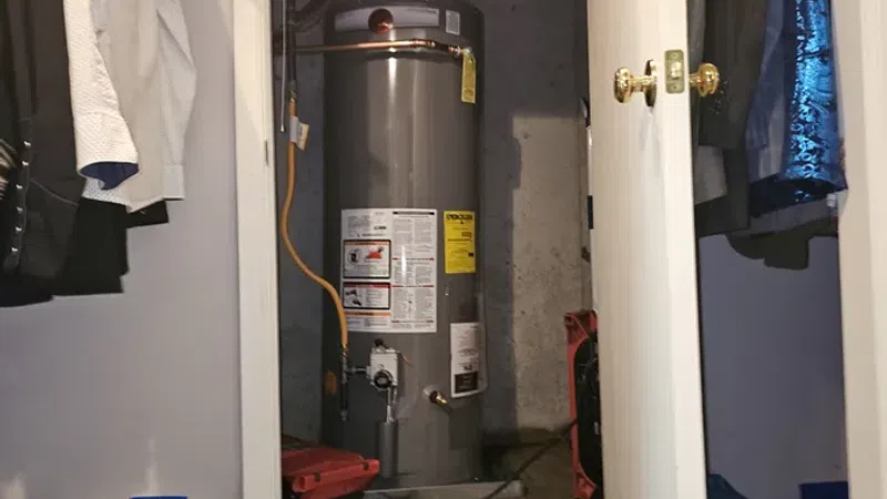 Water heater installed in a small closet with clothes hanging and maintenance equipment on the floor.