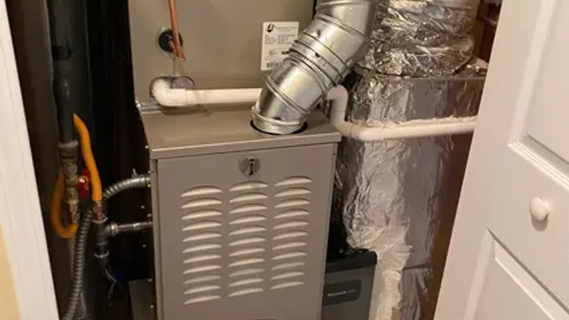 Carrier brand HVAC furnace unit with metallic ductwork and insulated pipes in a utility closet