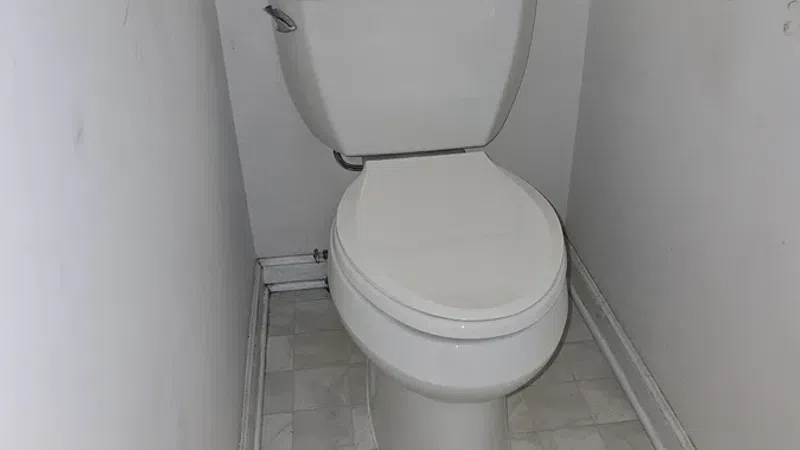White toilet installed in a small narrow bathroom with tiled floor and plain white walls.