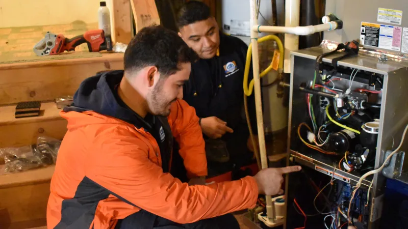 Technicians inspecting and repairing a residential furnace with tools in a basement setting