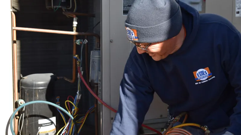 Technician in branded hoodie and beanie inspecting HVAC unit with wiring and copper pipes indoors