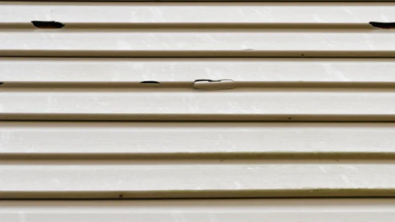Close-up of white metal siding with dents and peeling paint in horizontal panels.