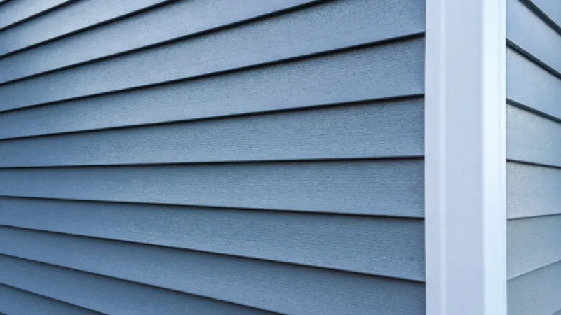 Close-up of blue vinyl siding on a house corner with white trim, showcasing texture and clean lines.
