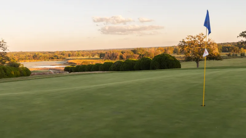 Golf green with blue flagstick overlooking a scenic autumn landscape at sunset