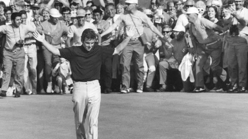 Golfer celebrating with arms raised on green as crowd cheers in historic black and white photo.