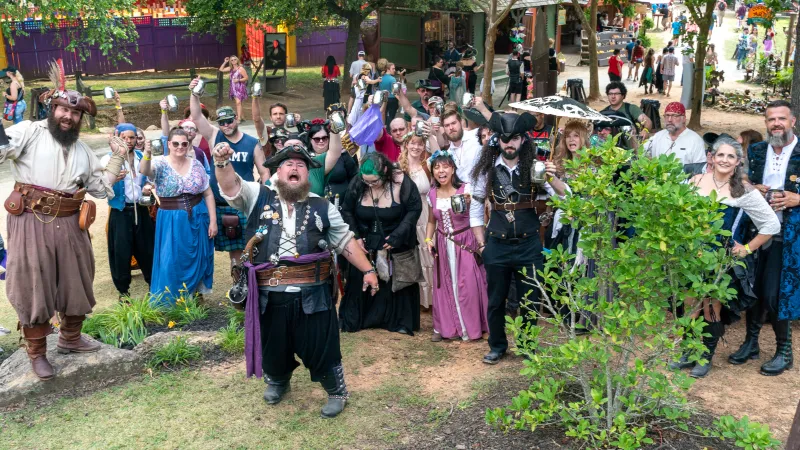 Group of people dressed as pirates celebrating outdoors at a festival with vibrant costumes and props.
