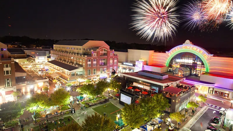 Nighttime city scene with fireworks above Regal Cinemas and bustling outdoor plaza filled with people and lights.