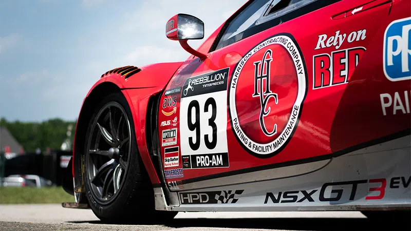 Close-up of red race car number 93 with sponsor logos and sleek alloy wheels on a sunny day.