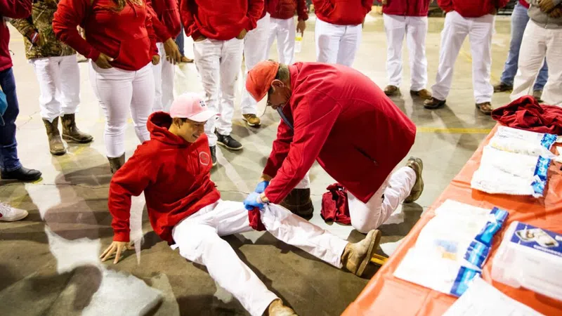 Group in red hoodies and white pants, one person helps seated man with leg injury indoors with medical supplies nearby