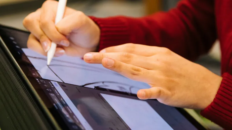 Person using a stylus to draw on a digital tablet with a red sweater visible in the background