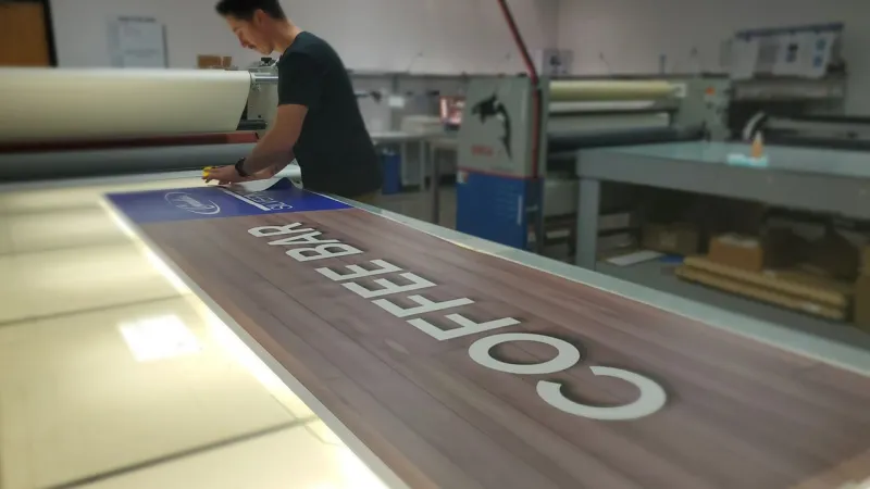 Worker preparing a large coffee bar sign with white letters on wood background in a print shop.