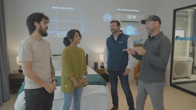 Four people discussing home comfort technology in a modern bedroom with temperature and noise visuals.