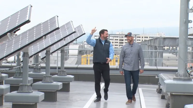 Two men walking and discussing on a rooftop with solar panels installed under an overcast sky