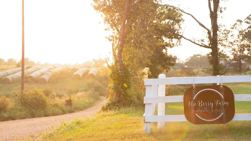 Sunny rural farm entrance with white fence and sign for The Berry Farm in Bentonville Arkansas