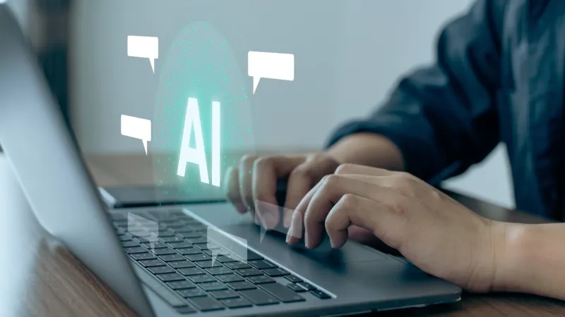 Person typing on laptop with holographic AI text and speech bubbles symbolizing artificial intelligence communication.