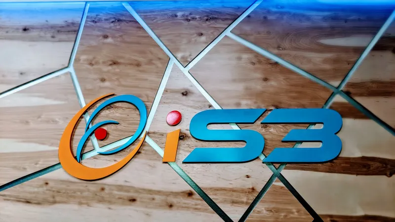 Colorful iS3 logo on a geometric wooden and glass background with blue lighting.