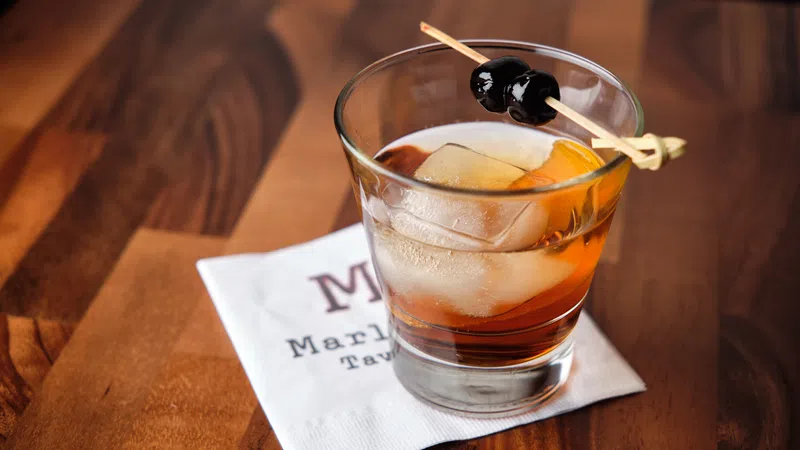 Old fashioned cocktail with large ice cube and cherries on a skewer on a wooden table with a napkin