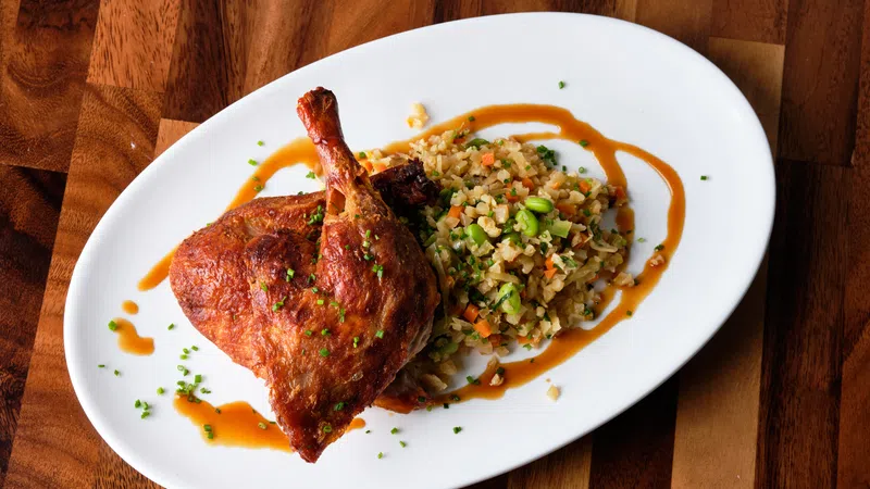 Crispy roasted chicken leg served with vegetable fried rice and drizzle of sauce on white plate