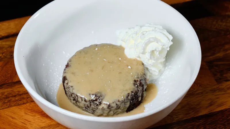 Chocolate dessert with creamy sauce and whipped cream served in a white bowl on wooden surface