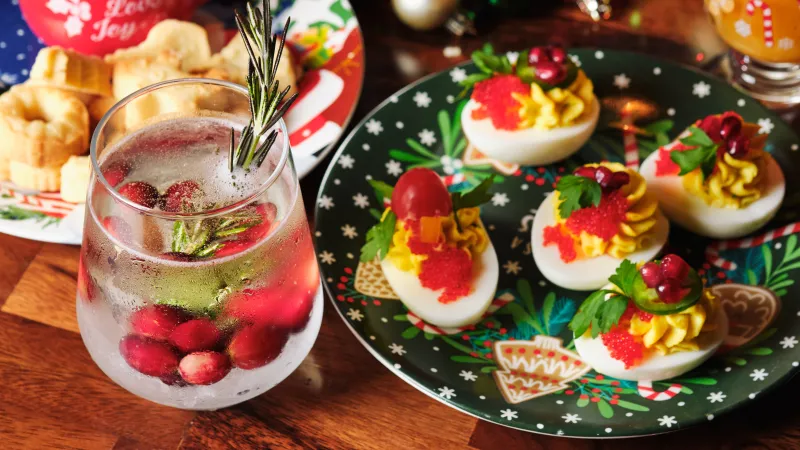 Festive holiday deviled eggs with herbs and red toppings on Christmas-themed plate and cranberry drink.