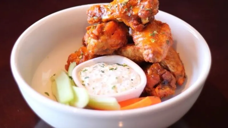 Spicy chicken wings served in a white bowl with ranch dressing and celery and carrot sticks.