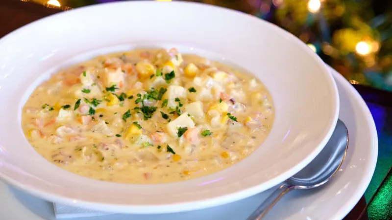 Bowl of creamy chowder garnished with parsley served with spoon, colorful bokeh lights in background.