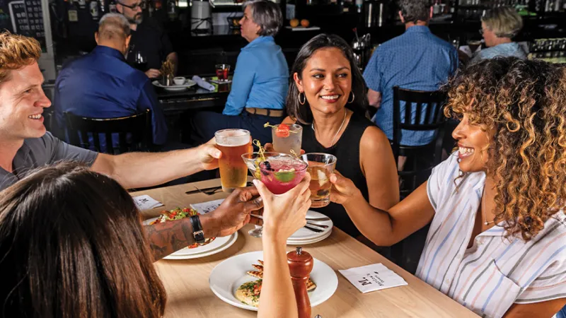 Group of friends enjoying drinks and food together at a lively restaurant table toast