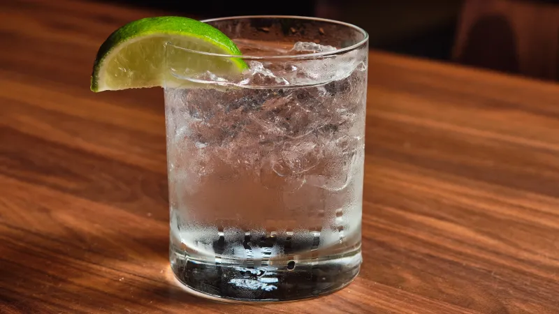Clear glass of iced water garnished with a lime wedge on a wooden surface with soft lighting.