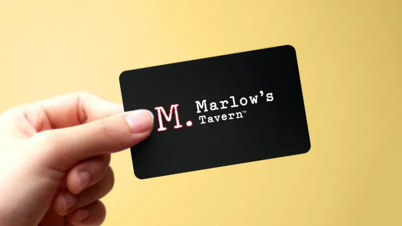 Hand holding a black business card with Marlow's Tavern logo on a yellow background