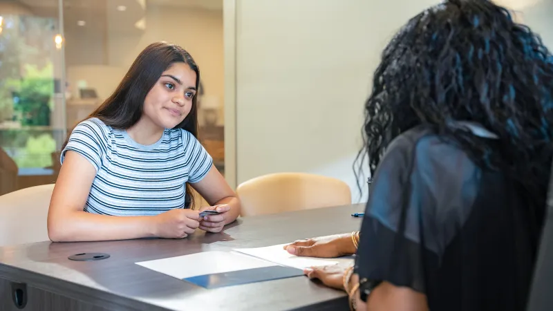 Young woman in striped shirt attentively listening during a meeting across a table with another person.