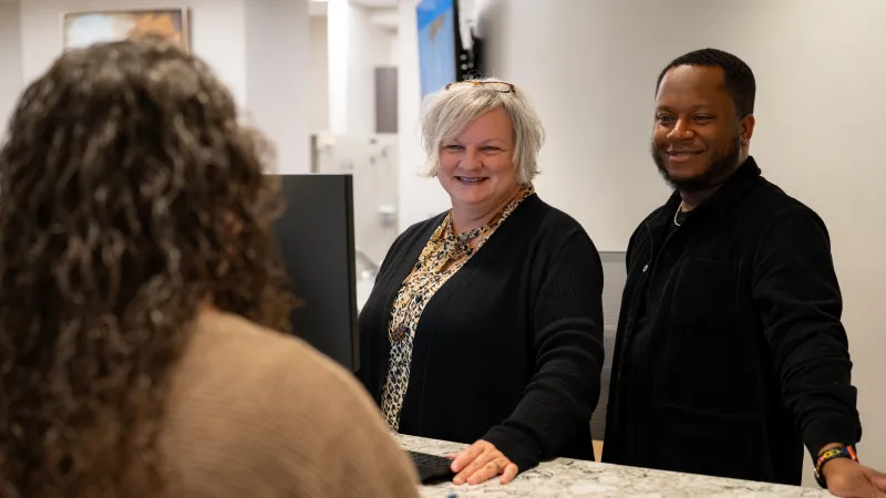 Two friendly receptionists assisting a visitor at a modern marble countertop in a bright office lobby