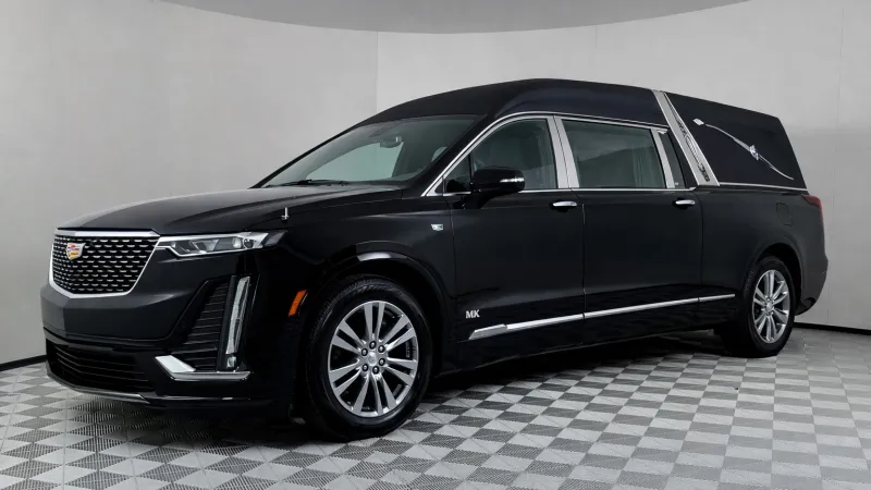Black Cadillac hearse with chrome detailing displayed on checkered floor background in showroom.