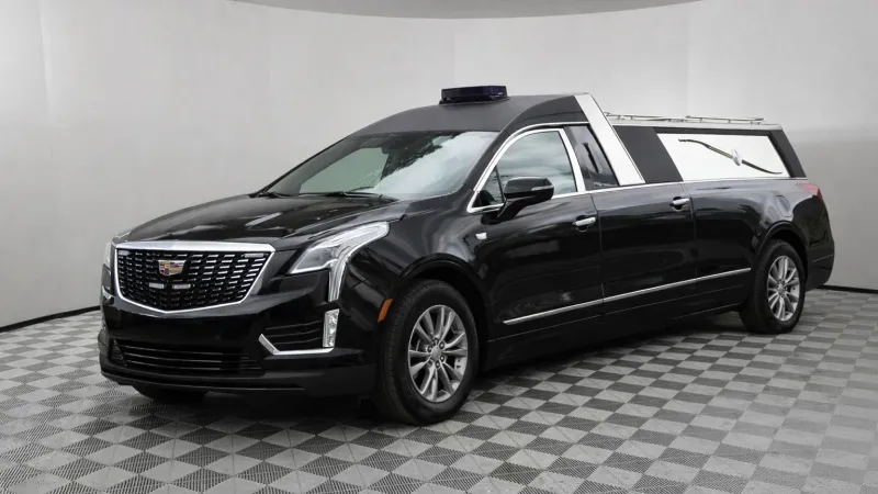 Black Cadillac hearse with extended rear and modern LED headlights on checkered showroom floor.