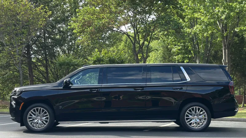 Black luxury extended limousine SUV parked in an outdoor setting with trees in the background