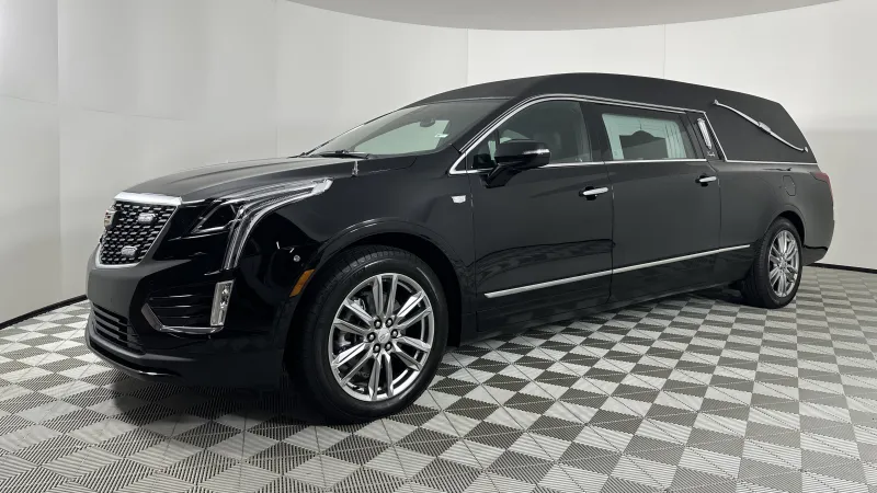 Black luxury Cadillac hearse with polished wheels in a white studio with patterned floor tiles.
