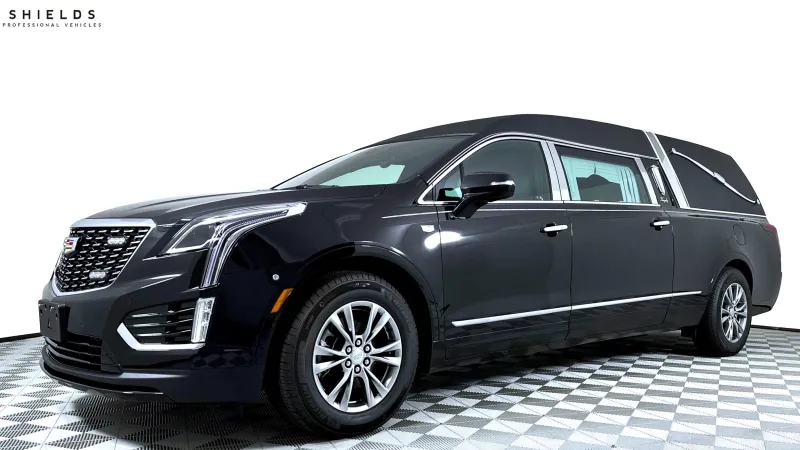 Black Cadillac hearse with sleek design, parked on a checkered floor.
