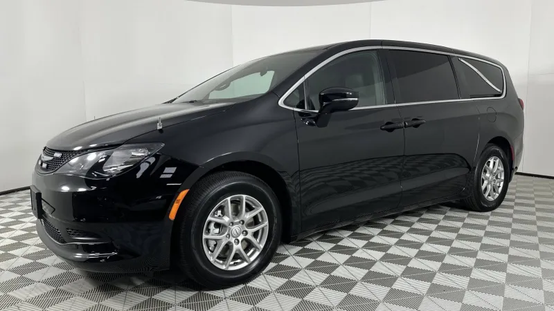 Sleek black minivan with tinted windows parked on checkered floor inside white studio space